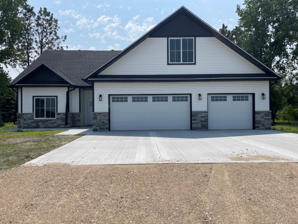 picture of the front of a new constructed house. The house has two garage doors in the center of the picture with the main door to the house being to the left of the garage doors.